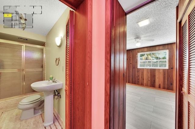 bathroom with wood walls, a shower with door, and a textured ceiling