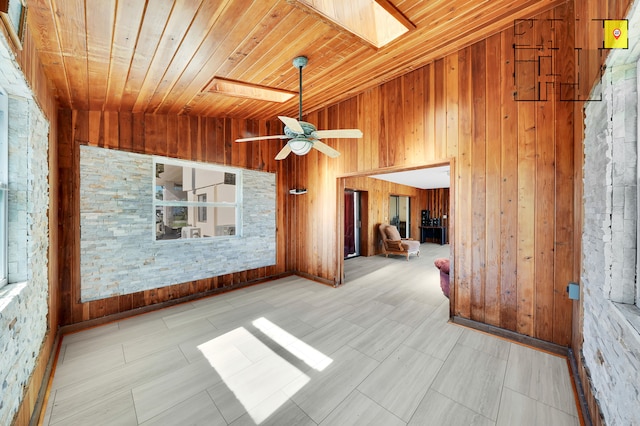 interior space with wood walls, vaulted ceiling with skylight, ceiling fan, and wood ceiling