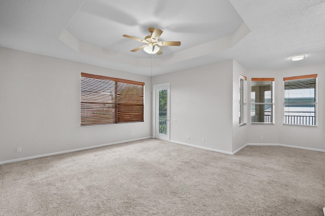 carpeted spare room featuring ceiling fan, a tray ceiling, and a healthy amount of sunlight