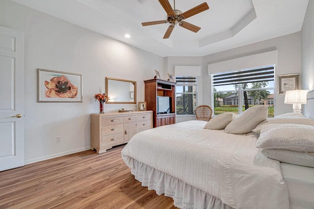 bedroom with light wood-type flooring, a tray ceiling, and ceiling fan