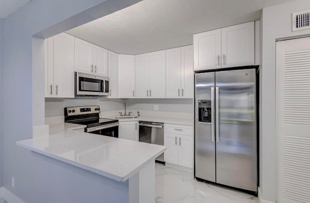 kitchen featuring kitchen peninsula, appliances with stainless steel finishes, light stone countertops, sink, and white cabinetry