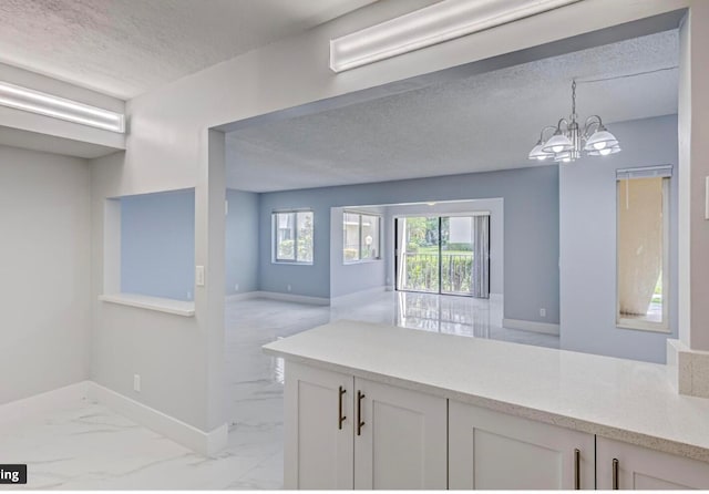 interior space with pendant lighting, a textured ceiling, white cabinetry, and a notable chandelier