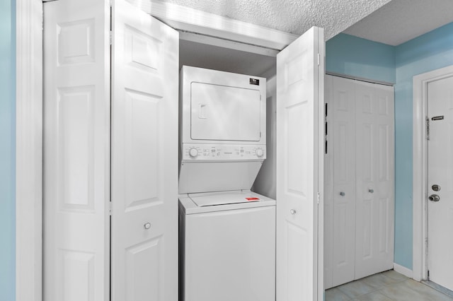 washroom with light tile patterned floors, a textured ceiling, and stacked washer and clothes dryer