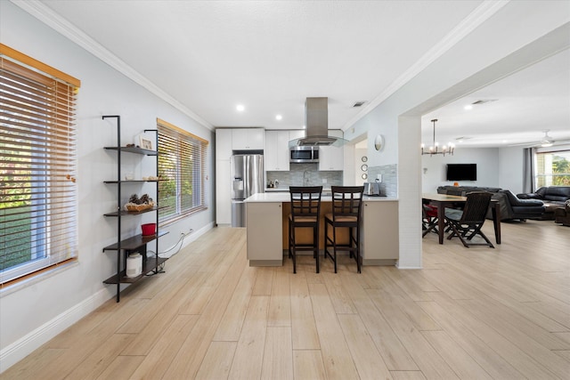 kitchen featuring a kitchen bar, appliances with stainless steel finishes, island range hood, white cabinets, and light hardwood / wood-style floors