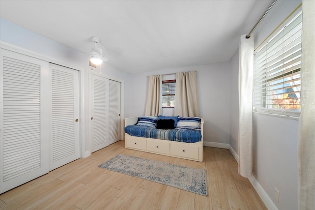 bedroom featuring ceiling fan, light hardwood / wood-style flooring, and two closets