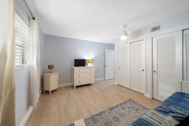 interior space featuring a textured ceiling, light wood-type flooring, two closets, and ceiling fan