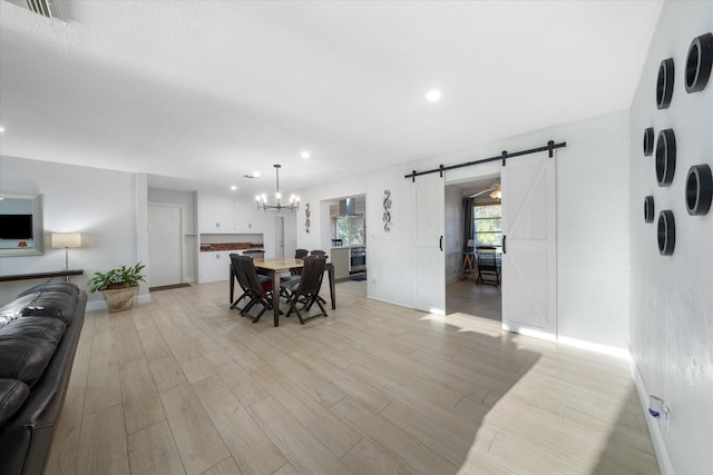 dining space with light wood-type flooring, a barn door, and an inviting chandelier