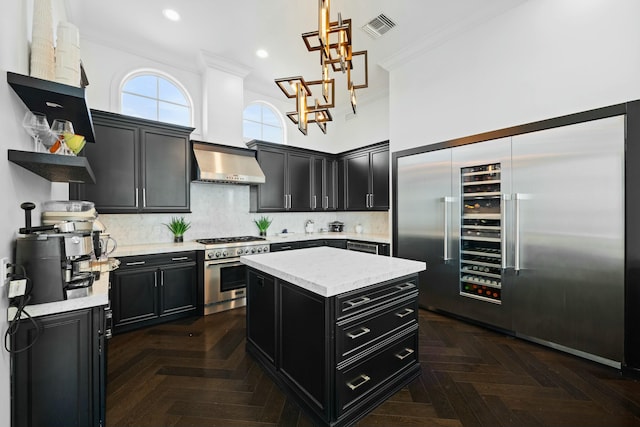 kitchen with a towering ceiling, premium appliances, dark parquet floors, wall chimney range hood, and a kitchen island