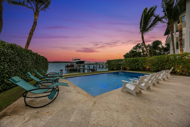 pool at dusk featuring a boat dock, a water view, and a patio area