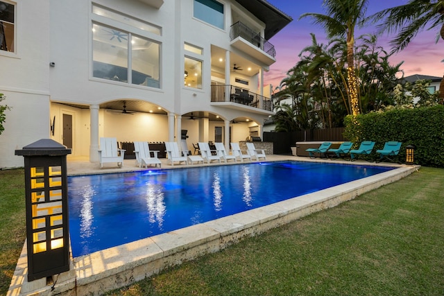 pool at dusk with a patio area and ceiling fan