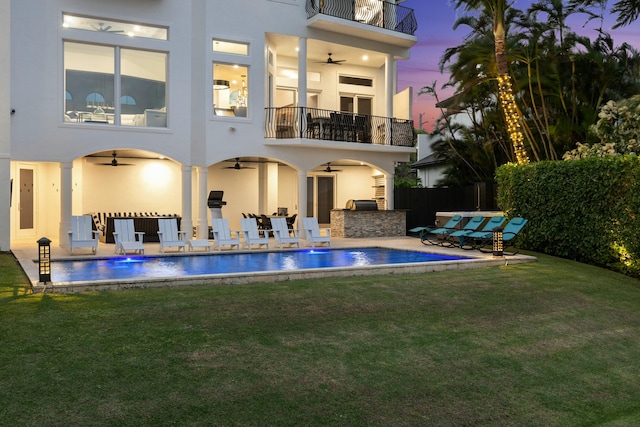 back house at dusk featuring a balcony, pool water feature, ceiling fan, a patio area, and a fenced in pool