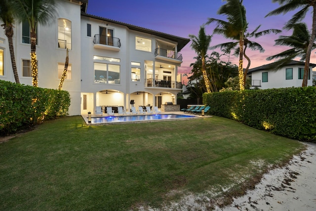 back house at dusk featuring a yard, a balcony, and a fenced in pool