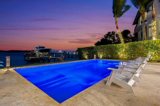 pool at dusk featuring a boat dock, a water view, and a diving board