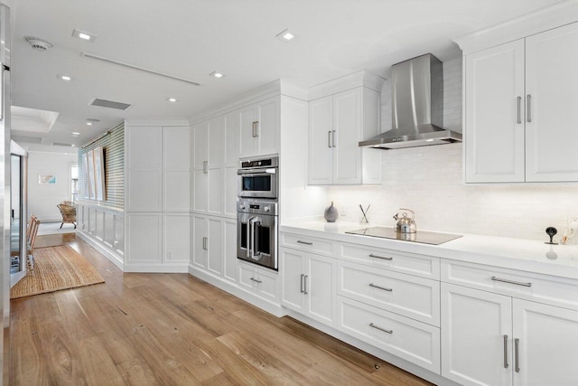 kitchen with white cabinets, wall chimney exhaust hood, black electric cooktop, and light hardwood / wood-style flooring