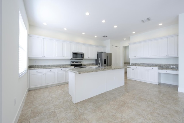 kitchen featuring sink, stainless steel appliances, light stone counters, a center island with sink, and white cabinets