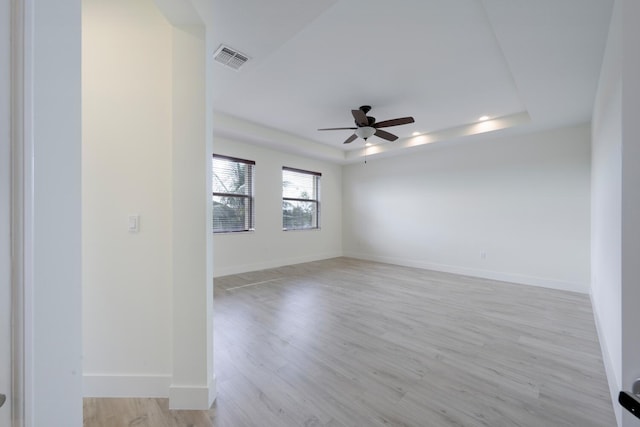 unfurnished room featuring a tray ceiling, ceiling fan, and light hardwood / wood-style floors