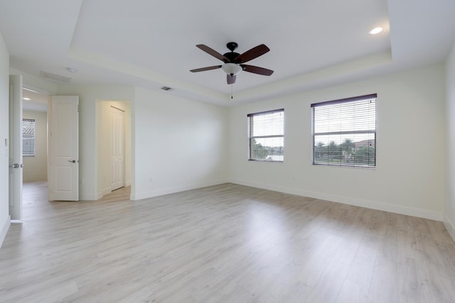 unfurnished room featuring light wood-type flooring, a tray ceiling, and ceiling fan