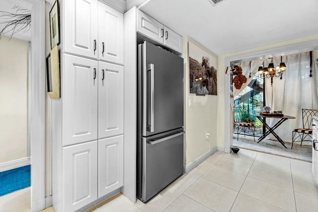 kitchen with stainless steel refrigerator, white cabinetry, light tile patterned floors, and a chandelier