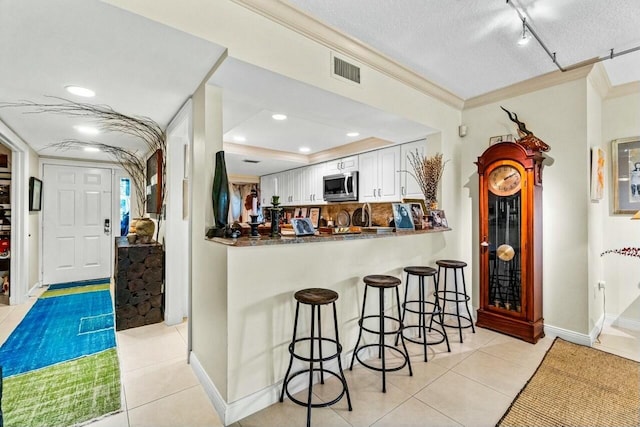 kitchen with light tile patterned floors, kitchen peninsula, a breakfast bar, white cabinets, and ornamental molding