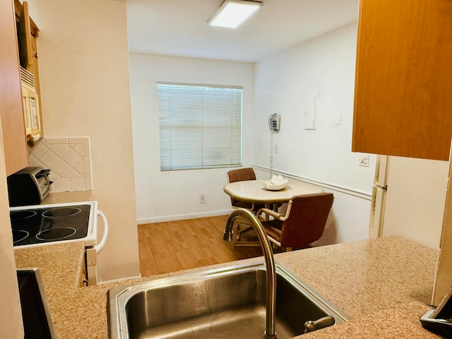 kitchen with hardwood / wood-style floors, light stone counters, range, and sink