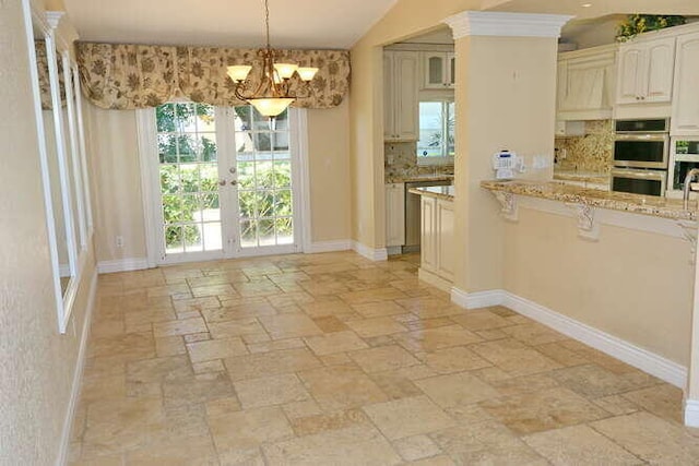 kitchen with light stone countertops, stainless steel double oven, a notable chandelier, lofted ceiling, and decorative light fixtures