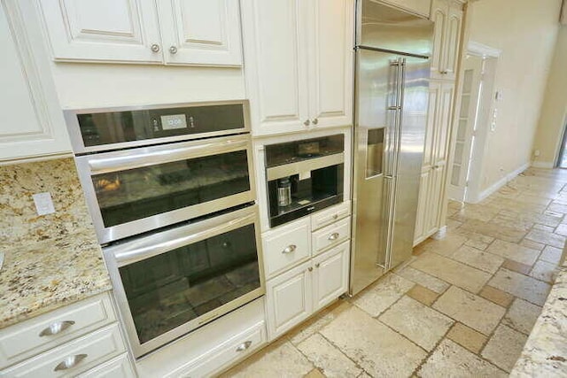 kitchen with built in appliances, light stone countertops, and white cabinets