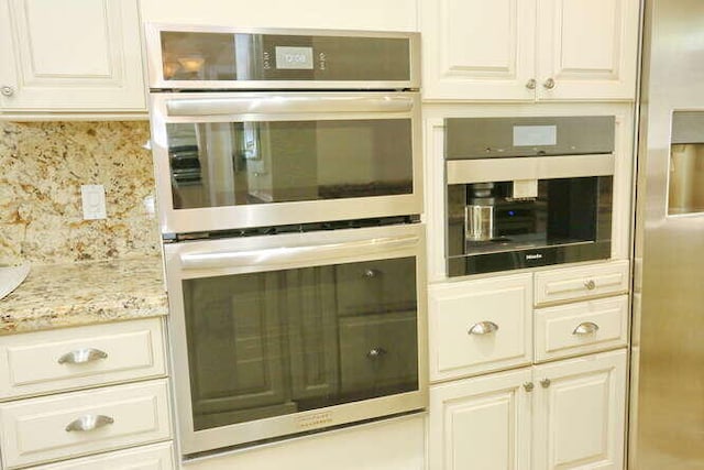 kitchen featuring decorative backsplash, stainless steel double oven, white cabinets, and light stone counters