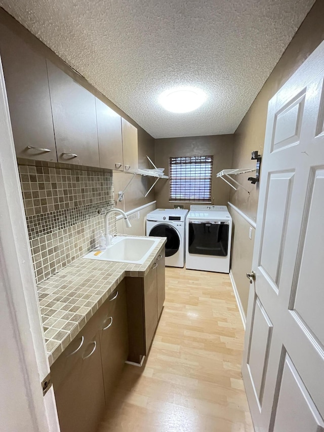 laundry room featuring sink, cabinets, a textured ceiling, washer and dryer, and light wood-type flooring