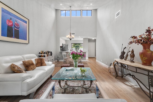 living room with a high ceiling, a chandelier, and light hardwood / wood-style flooring