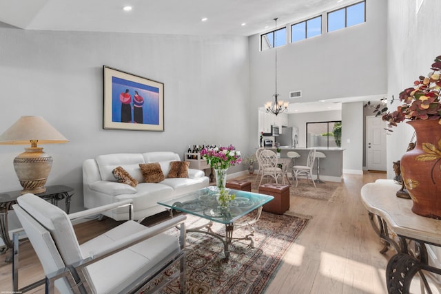 living room with light hardwood / wood-style flooring, a towering ceiling, and a chandelier