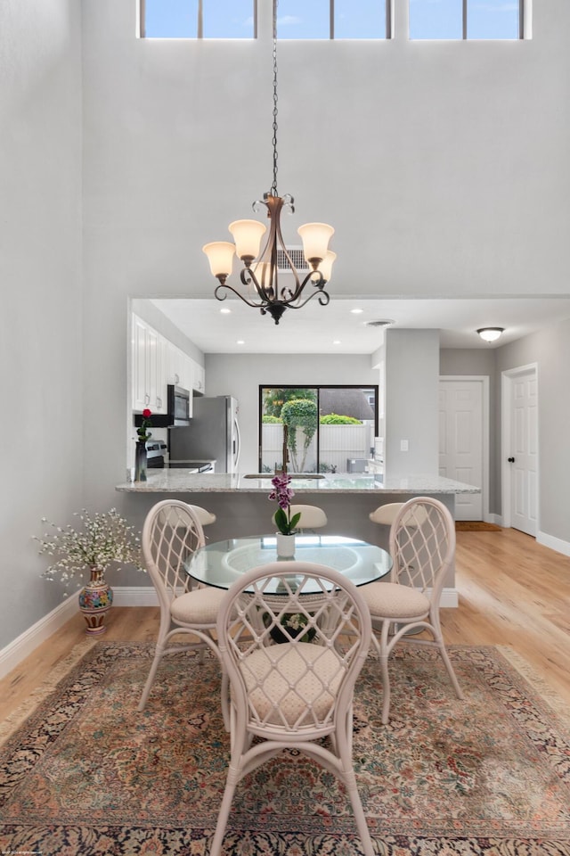 dining room with a high ceiling, light wood-type flooring, and an inviting chandelier