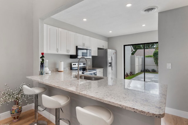 kitchen with stainless steel appliances, white cabinets, a kitchen breakfast bar, light wood-type flooring, and kitchen peninsula