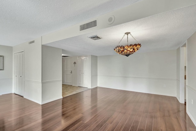 empty room with hardwood / wood-style floors, a textured ceiling, and an inviting chandelier