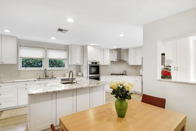 kitchen featuring white cabinets, wall chimney range hood, sink, and stainless steel appliances