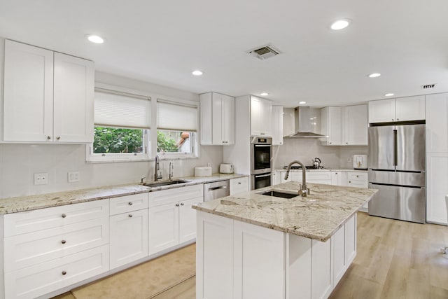 kitchen featuring white cabinetry, sink, wall chimney range hood, a kitchen island with sink, and appliances with stainless steel finishes