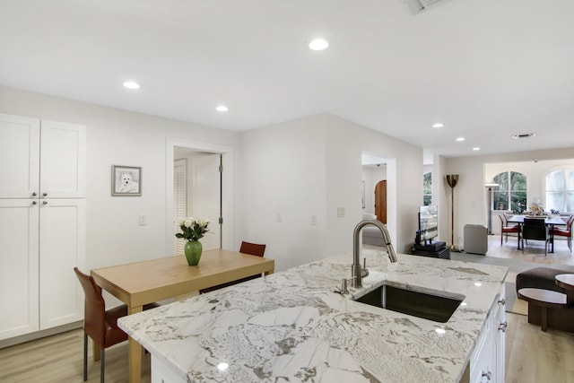 kitchen featuring white cabinets, light wood-type flooring, a center island with sink, and sink