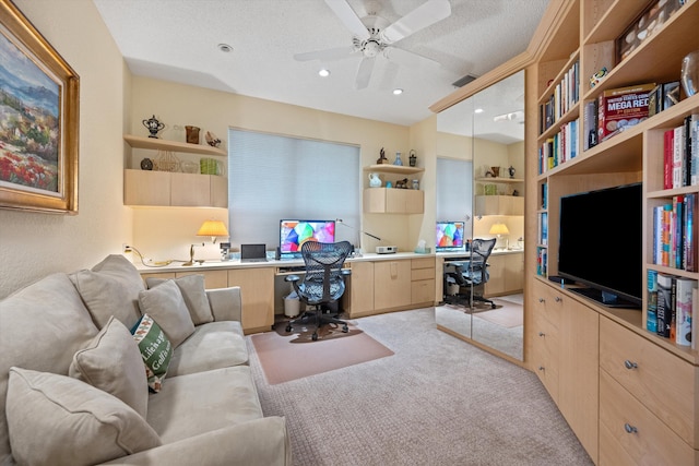 carpeted home office with a textured ceiling, ceiling fan, and built in desk