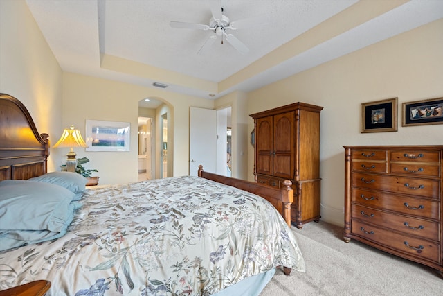 bedroom with ceiling fan, light carpet, connected bathroom, and a tray ceiling