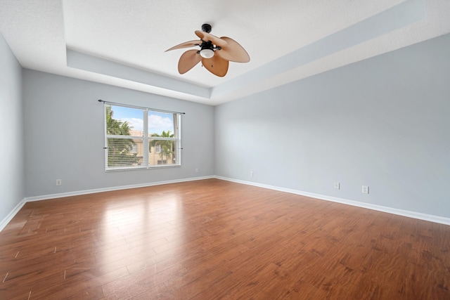 spare room with ceiling fan, wood-type flooring, and a tray ceiling