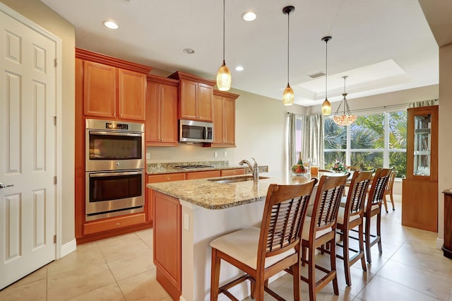 kitchen featuring sink, decorative light fixtures, a center island with sink, a tray ceiling, and stainless steel appliances