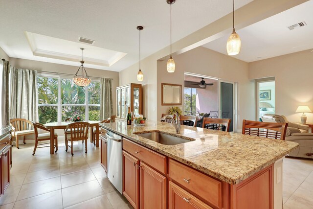 kitchen with light stone countertops, sink, stainless steel appliances, decorative light fixtures, and a center island with sink