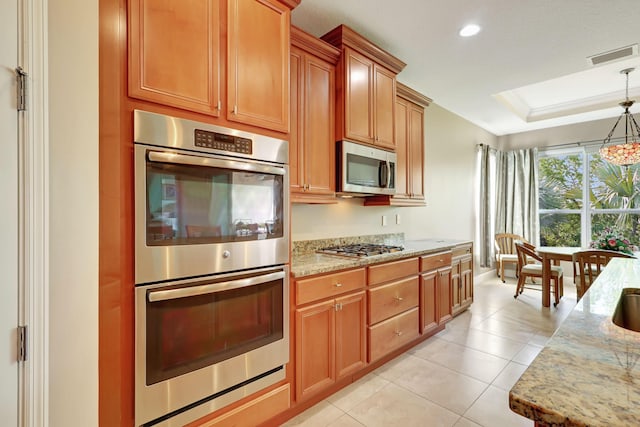 kitchen featuring light stone counters, decorative light fixtures, light tile patterned floors, a tray ceiling, and stainless steel appliances