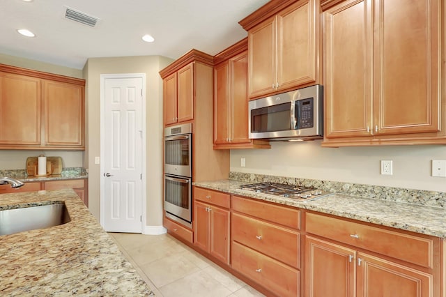 kitchen featuring stainless steel appliances, sink, light tile patterned floors, and light stone counters