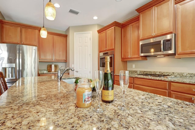 kitchen featuring pendant lighting, sink, light stone counters, and appliances with stainless steel finishes