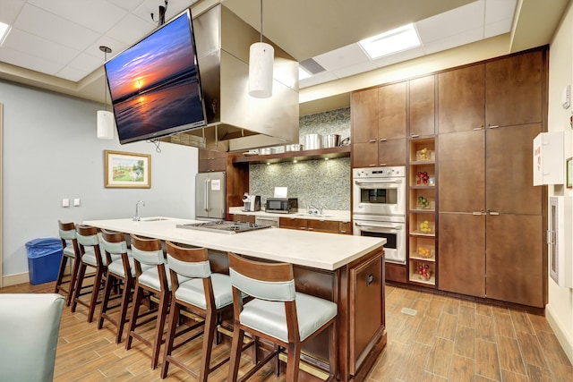 kitchen featuring decorative backsplash, light wood-type flooring, a paneled ceiling, a breakfast bar, and stainless steel appliances