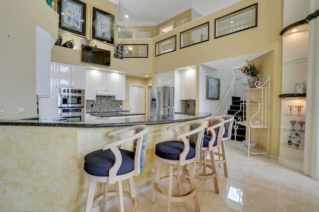 kitchen featuring kitchen peninsula, crown molding, dark stone countertops, white cabinets, and a high ceiling