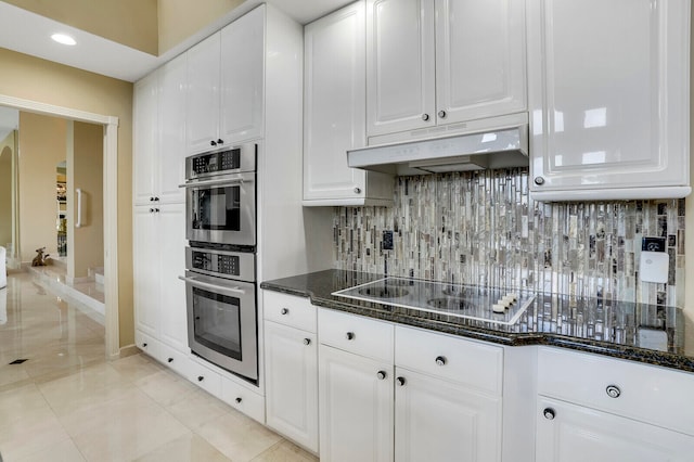 kitchen featuring backsplash, stainless steel double oven, light tile patterned floors, dark stone countertops, and white cabinetry