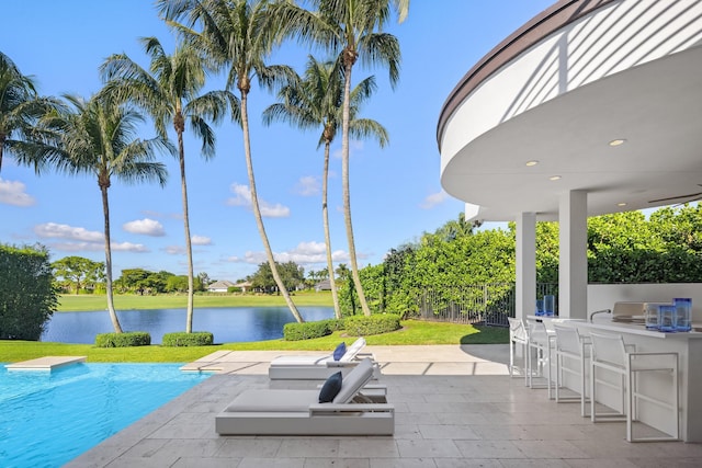 view of swimming pool with a lawn, a water view, an outdoor bar, and a patio