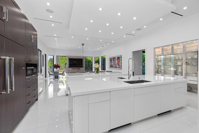 kitchen featuring light tile patterned floors, white cabinetry, sink, and a large island with sink