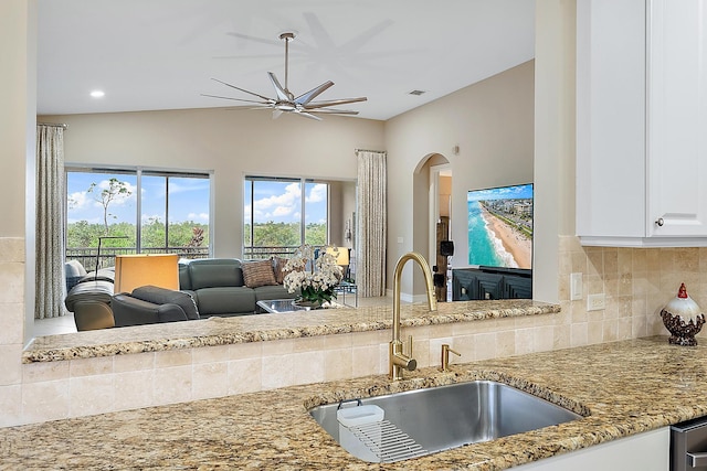 kitchen featuring light stone countertops, backsplash, vaulted ceiling, sink, and white cabinets